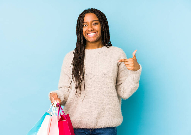 Νεαρή Αφροαμερικάνα που κρατάει μια τσάντα για ψώνια, απομονωμένη, δείχνοντας με το χέρι ένα χώρο για φωτοτυπίες, περήφανη και σίγουρη. - Φωτογραφία, εικόνα