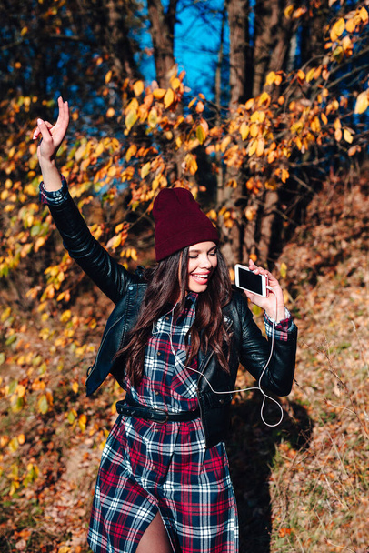 Beautiful girl listening to music on smartphone and dancing in autumn park - Foto, imagen