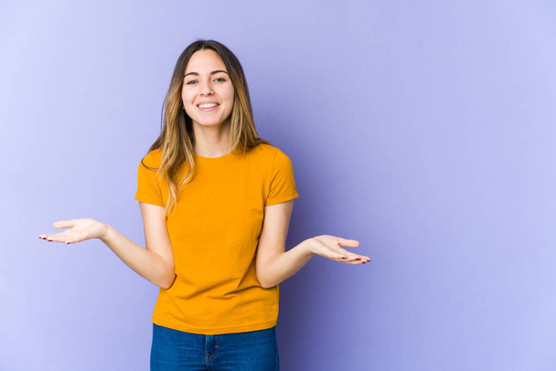 Young caucasian woman isolated on purple background makes scale with arms, feels happy and confident. - Photo, Image