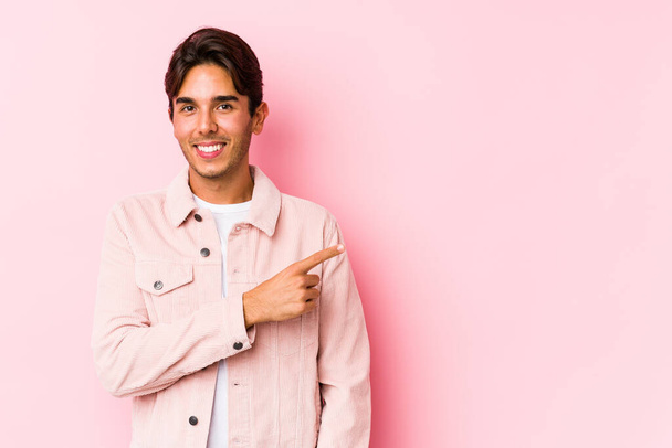 Young caucasian man posing in a pink background isolated smiling and pointing aside, showing something at blank space. - Photo, Image