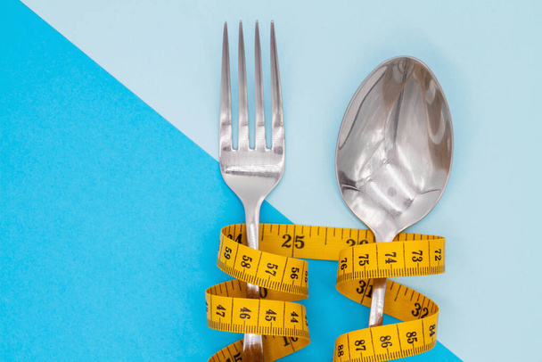 Fork and spoon is strung by a ribbon for measuring on a colored background. Symbol of diet and weight loss - 写真・画像