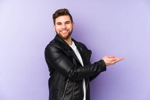 Young man isolated on purple background holding a copy space on a palm. - Photo, Image