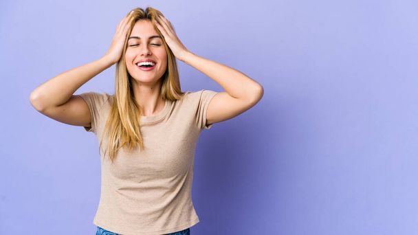 Young blonde woman isolated on purple background laughs joyfully keeping hands on head. Happiness concept. - Photo, Image