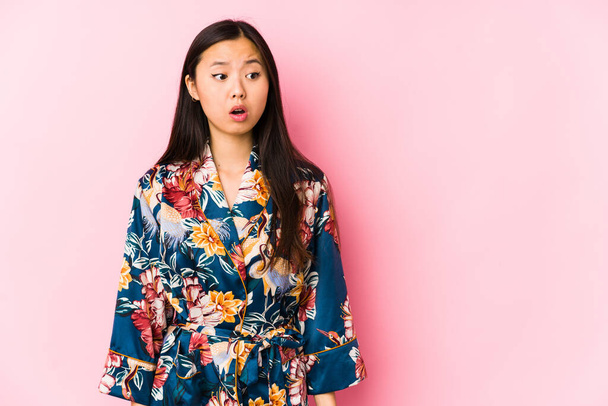 Jeune femme chinoise portant un pyjama kimono isolé étant choquée à cause de quelque chose qu'elle a vu. - Photo, image