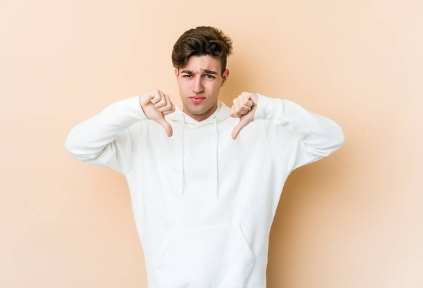 Young caucasian man isolated on beige background showing thumb down, disappointment concept. - Photo, Image