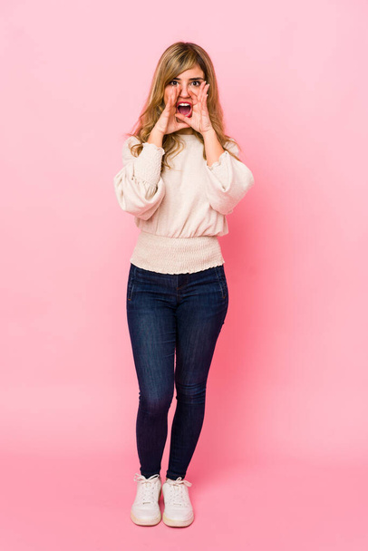 Young blonde caucasian woman standing over a pink background shouting excited to front. - Fotografie, Obrázek
