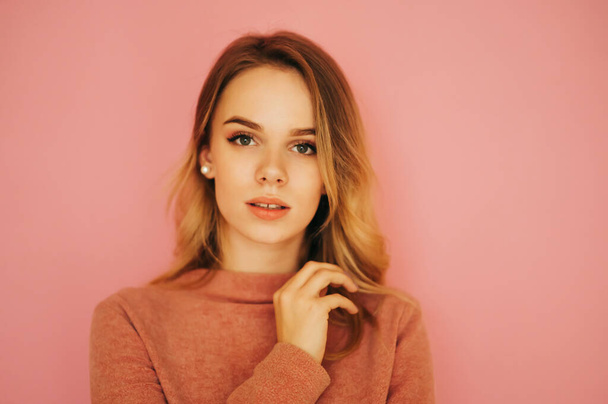 Attractive woman in a pink sweater stands on a pink background and poses for the camera with a sexy face. Copy space. - Fotoğraf, Görsel