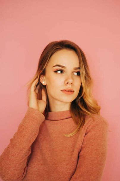Sexy woman in a pink sweater isolated on a pink background, pensively looking away with a serious face. Copy space. Close portrait of a blonde - 写真・画像