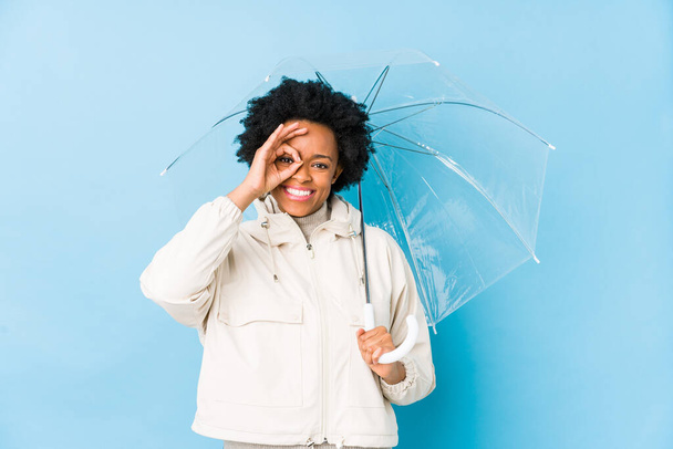 Mladá africká americká žena drží deštník izolované vzrušení udržet ok gesto na oku. - Fotografie, Obrázek
