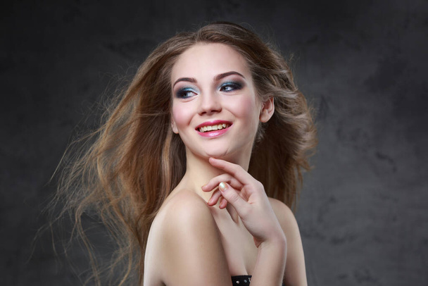 Beauty portrait of a happy smiling girl with bright makeup and long hair developing in the wind isolated on a gray background. - Foto, immagini