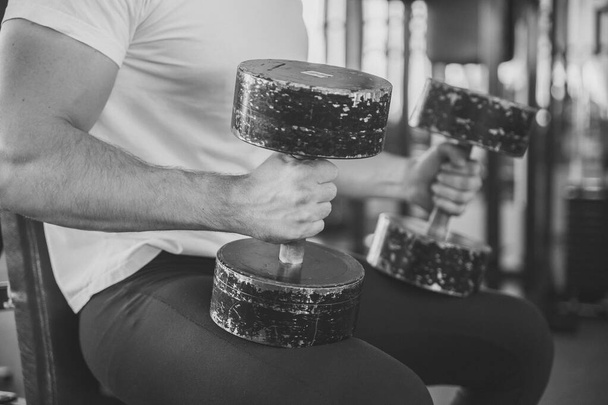 black and white photo of an athlete with old dumbbells in his hands focus on the foreground - Photo, Image