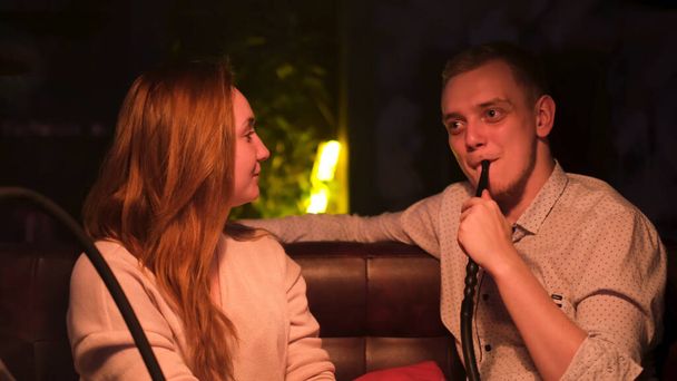 Mężczyzna i kobieta na randce w barze Hookah palący i gadający. Media. mężczyzna palacz słuchać jego dziewczyna uważnie podczas palenie shisha w ciemnym świetle. - Zdjęcie, obraz