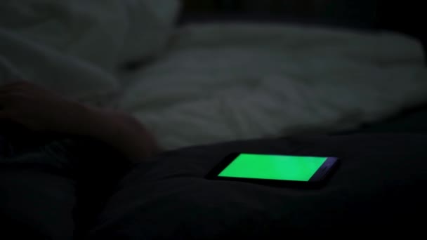 Κοντινό πλάνο ψηφιακού κινητού με πράσινη οθόνη και έναν άντρα στο κρεβάτι. Έννοια. Ύπνος άνθρωπος που χρησιμοποιεί το smartphone του και προσπαθεί να κοιμηθεί, έννοια της εξάρτησης από το τηλέφωνο και αϋπνία. - Πλάνα, βίντεο