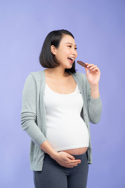 Portrét šťastné těhotné ženy s čokoládovou tyčinkou stojící nad fialovou - Fotografie, Obrázek
