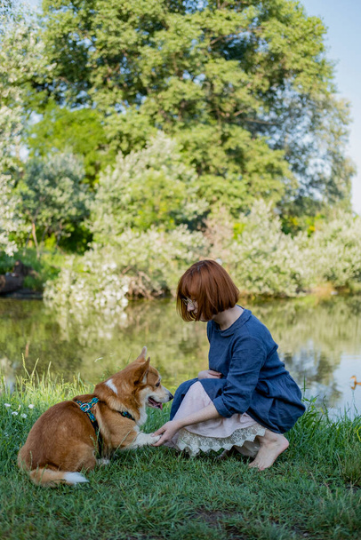 Young woman walk in the park near river with cute corgi dog - Fotó, kép