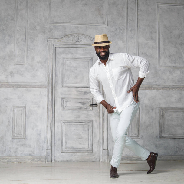 Black elegant man in a white suit and hat is dancing in a bright room near the door. - Fotoğraf, Görsel