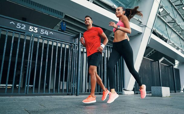 Full length of confident young man and woman in sports clothing running and smiling while practicing outdoors - Фото, изображение