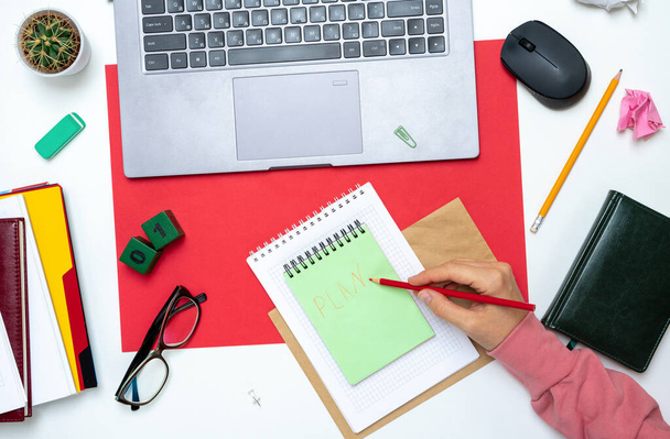 Makieta Workspace widok góry na czerwonym tle z notatnikiem, długopisem, okulary, laptop i akcesoria. Ręce kobiety jedzą plan na początku miesiąca. - Zdjęcie, obraz