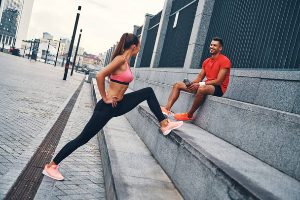 Beautiful young couple in sports clothing warming up and stretching while practicing outdoors on the city street - Φωτογραφία, εικόνα