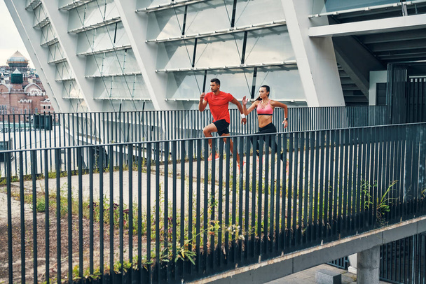 Full length of young beautiful couple in sports clothing enjoying morning jogging while practicing outdoors - Valokuva, kuva