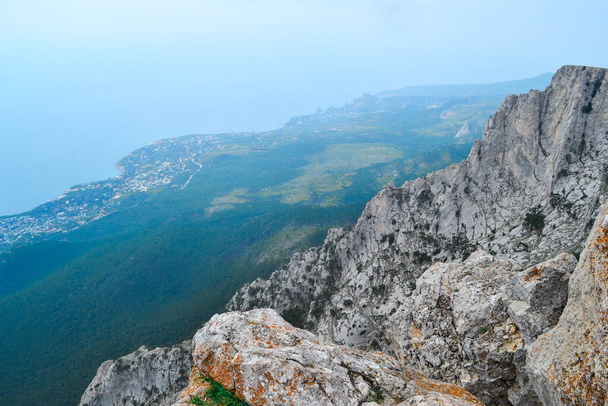 view of large steep stone rock cliff against the backdrop of blue sea coastline with city and forest - Φωτογραφία, εικόνα
