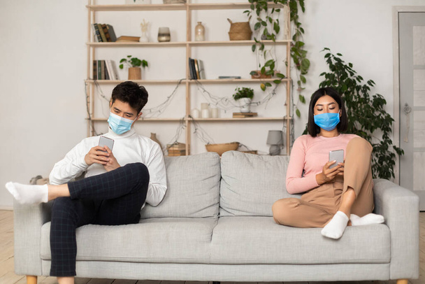 Asijské manželé v lékařských maskách textové pomocí smartphonů doma - Fotografie, Obrázek
