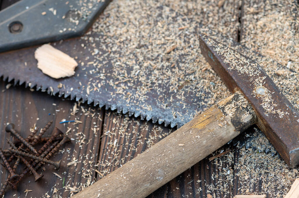 Old vintage hammer, wood saw, nails and sawdust on a wooden background, close-up, selective focus - 写真・画像