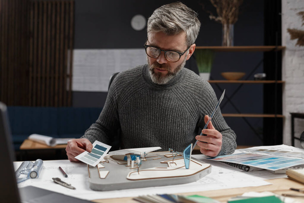 3d architect working in office with color palette. Designer select colors for building using color swatches, searching new ideas for construction project. Portrait of handsome bearded man at workplace - Fotó, kép