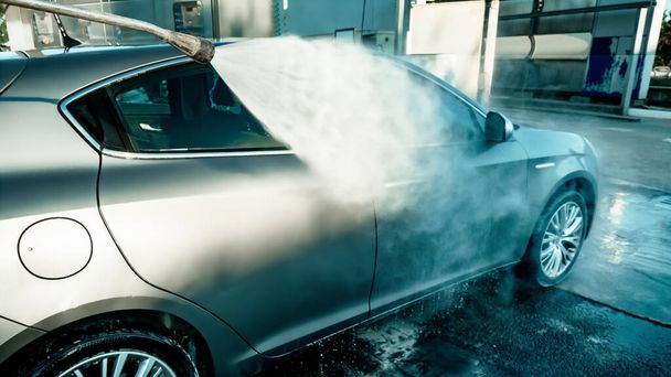 Μη αναγνωρισμένος άνθρωπος πλένει γκρι όχημα σε πλυντήριο αυτοκινήτων με νερό υψηλής πίεσης. Καθαρίζω το μηχάνημα. Αυτοεξυπηρέτηση - Φωτογραφία, εικόνα