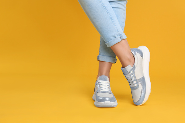 Woman wearing stylish sneakers on yellow background, closeup. Space for text - Zdjęcie, obraz