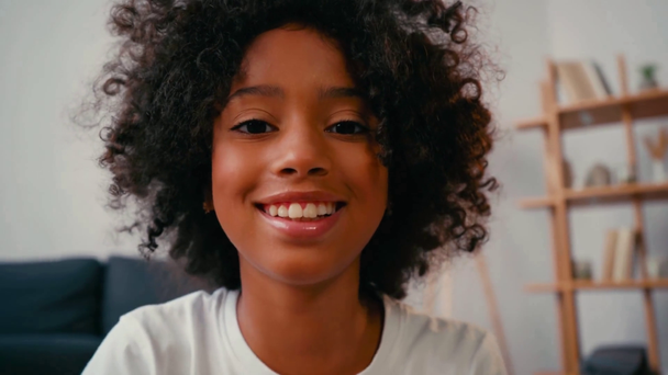 Enfoque selectivo de chica afroamericana sonriendo y mirando a la cámara en casa - Imágenes, Vídeo