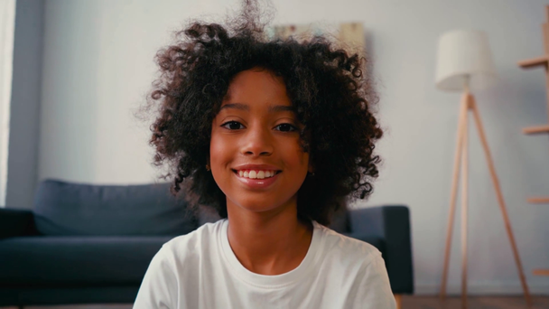 Selektywne skupienie się na uśmiechniętej afrykańskiej dziewczynie patrzącej przed kamerą w domu - Materiał filmowy, wideo