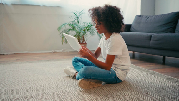 Oldalnézet afro-amerikai lány ül a szőnyegen, és használja a digitális tabletta - Felvétel, videó