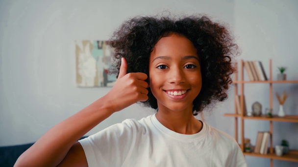 Szelektív fókusz afro-amerikai lány hüvelykujjával felfelé néz kamera otthon - Felvétel, videó