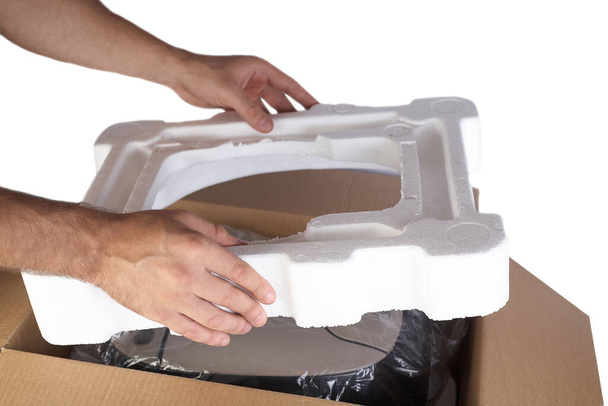 Packing goods in cardboard box with styrofoam material for safe transportation of cargo. Isolated on white background. Man's hands are packing the goods. - Photo, Image