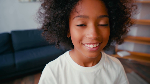 Enfoque selectivo de chica afroamericana sonriendo y mirando a la cámara en casa - Imágenes, Vídeo