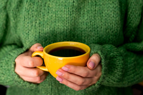 暖かい緑色のセーターの女性の手はコーヒーを一杯持っています - 写真・画像