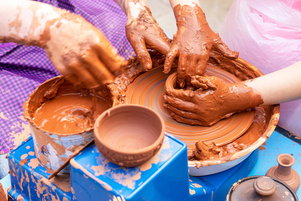 Master ceramist teaches student.Master ceramist teaches student. Craftsman hands making pottery bowl. Woman working on potter wheel . Family business shop sculpts pot from clay view top. - Photo, Image