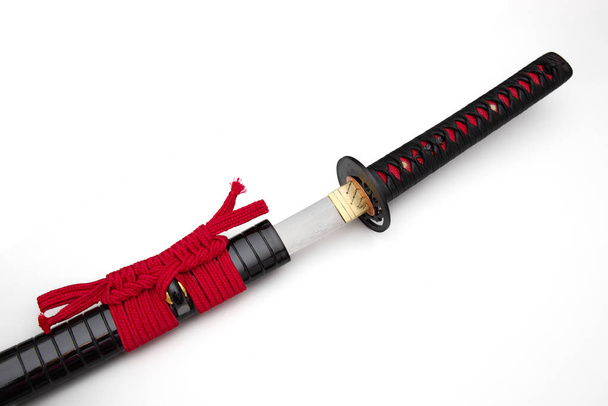 Japanese sword with red cord   steel fitting and shiny black scabbard on white background. Selective focus. - Photo, Image