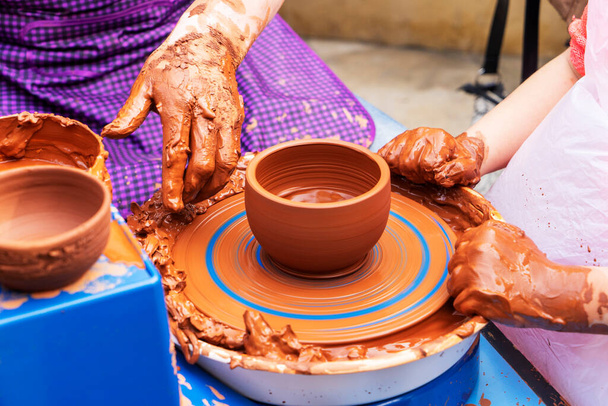 陶芸家は学生に教える陶芸家は学生に教える。陶器の器を作る職人の手。ろくろで働く女。土の上から見た家族経営の店の彫刻鍋. - 写真・画像