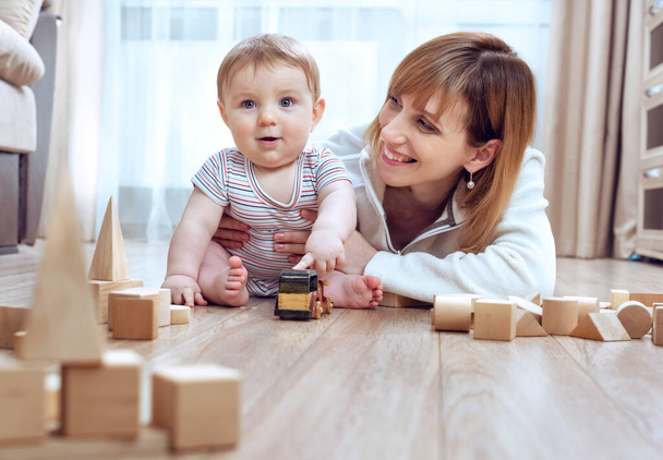 Lying on warm wooden floor mom play game with little son holds construction blocks. Spend time have fun together educational activity with kid concept. comfort house. - Photo, Image