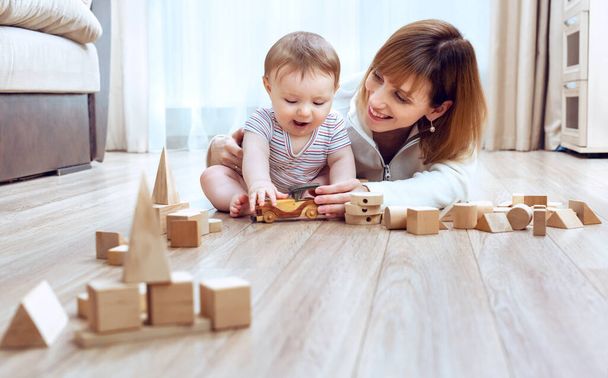 Auf warmem Holzboden liegend spielt Mama mit ihrem kleinen Sohn ein Spiel mit Bauklötzen. Verbringen Sie Zeit mit Spaß zusammen pädagogische Aktivität mit Kinderkonzept. Fußbodenheizung - Foto, Bild