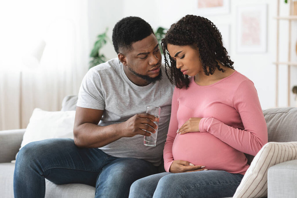 Femme enceinte noire se sentant malade, mari donnant un verre d'eau - Photo, image