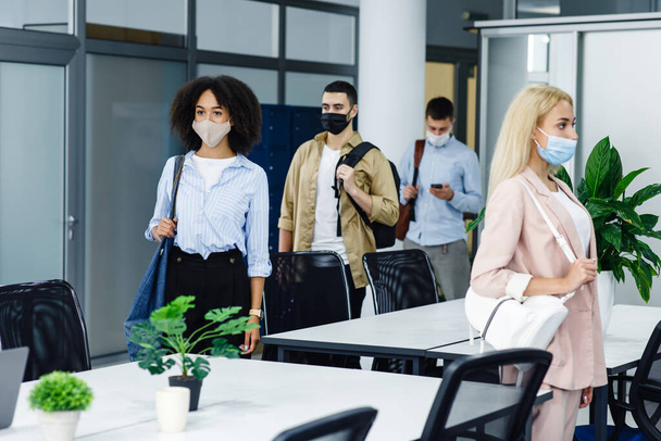 Health protection and return to work after quarantine covid-19. Multiracial young employees in protective masks go to workplaces in morning in modern office - Photo, Image