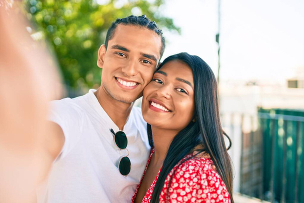Νεαρό ζευγάρι Λατίνων χαμογελά χαρούμενος κάνοντας selfie από την κάμερα στο δρόμο της πόλης. - Φωτογραφία, εικόνα