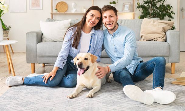 Mladí šťastní manželé se psem sedí v obývacím pokoji - Fotografie, Obrázek