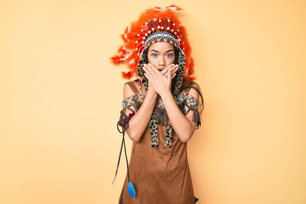 Joven hermosa chica latina con traje indio impactado cubriendo la boca con las manos por error. concepto secreto.  - Foto, imagen