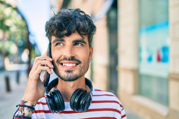 Молодий іспаномовний чоловік в навушниках і розмовляє по смартфону на вулиці міста
 - Фото, зображення
