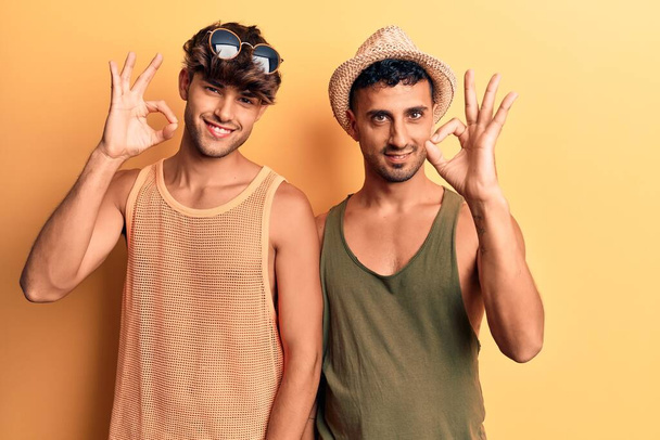 Mladý gay pár v letních šatech s pozitivním úsměvem dělá dobře znamení s rukou a prsty. úspěšný výraz.  - Fotografie, Obrázek