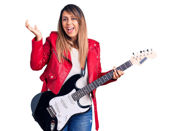 Young beautiful woman playing electric guitar celebrating victory with happy smile and winner expression with raised hands  - Foto, imagen